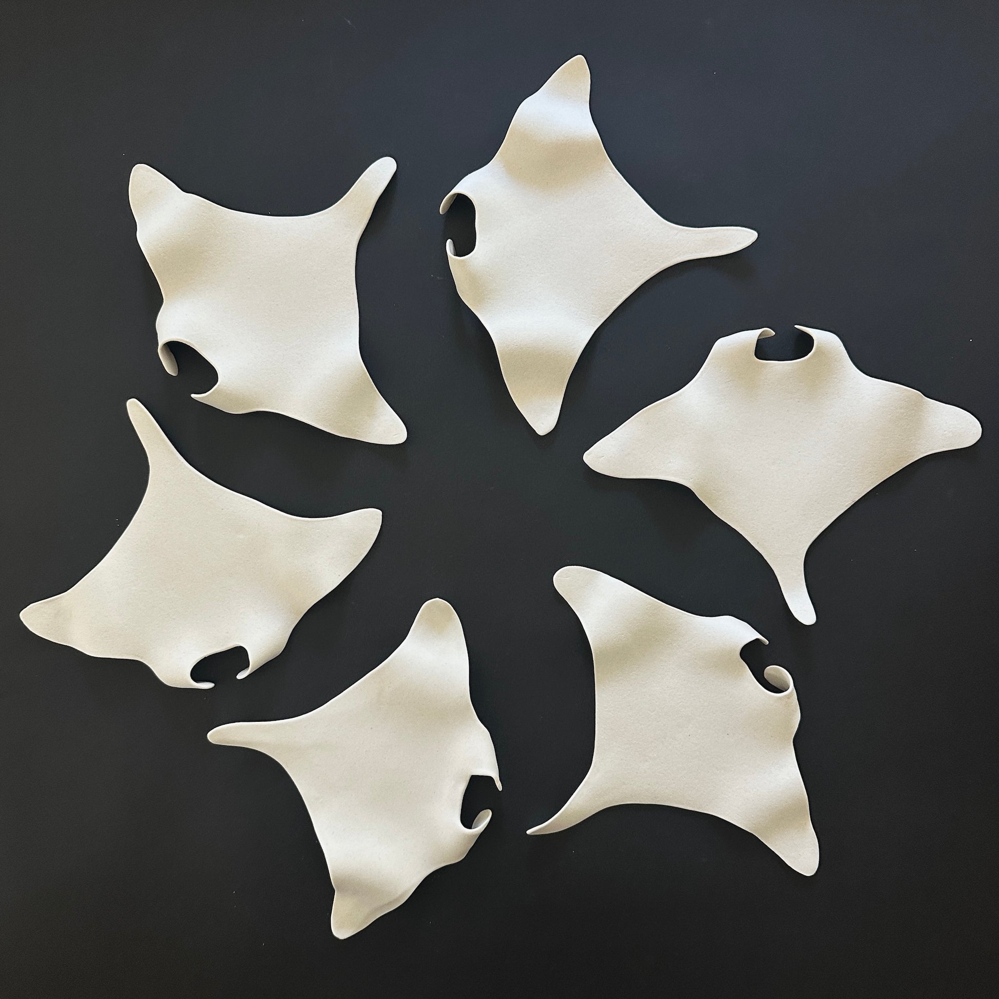 A collection of white porcelain wall decor items in the shape of manta rays arranged on a black background.